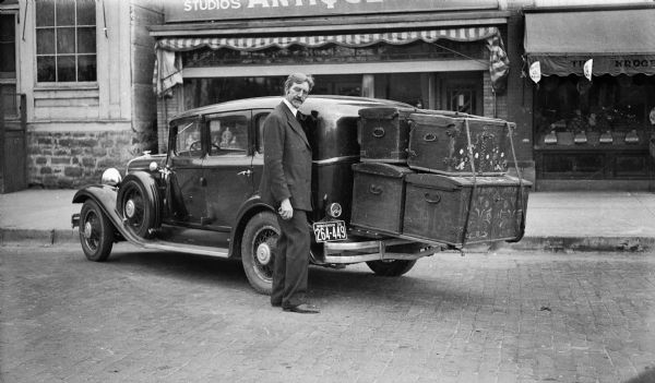 Ephraim Trimpey standing with a car loaded with four large trunks.