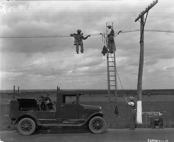 Two telephone line repair men hanging from a line, one of them on a ladder.