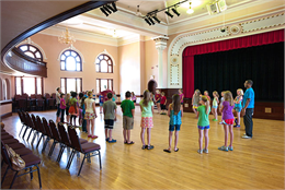 Interior of Heyde Center for the Arts. Group of school children standing in a circle in the former high school gym learning about theater.
