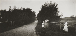 Ada Bass leaning against a fence, next to Everetta Bass as a young girl, along a dirt road. Another unidentified woman is also leaning against a fence.
