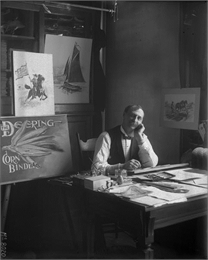International Harvester advertising artist sitting at his desk in a studio office with a wistful look on his face. Graphics from Deering brand advertisements are propped up behind him. The photo was likely taken at the company's McCormick Works.