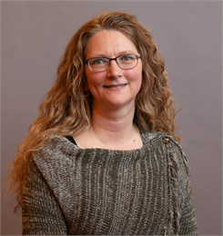 Photograph of Rose Haveri, a woman with curly hair and glasses, wearing a knitted top