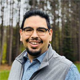 Photograph of Dan Soulier, a black-haired man wearing a grey vest, floral shirt, and glasses