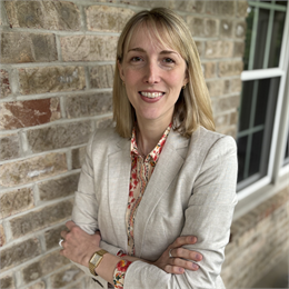 Photograph of Kristen Leffelman, a blonde woman wearing a floral shirt and beige blazer
