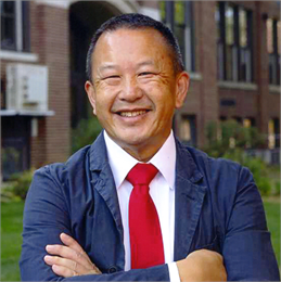 Headshot of Pao Lor wearing a suit and smiling outside the UW-Green Bay campus.