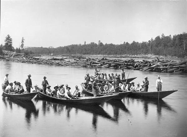 Five bateaux, or boats, with loggers in them.In the background on the left is a bridge.