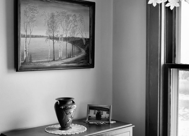 A vase on a dresser near a window with lace curtains.