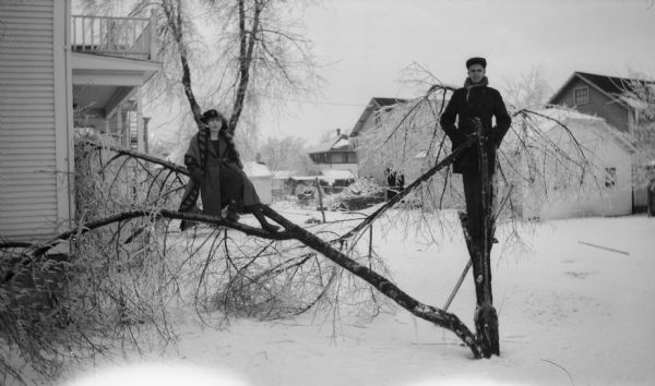 Harman Warner and Ethel Walker pose in the branches of a broken tree in winter. They are in the backyard, and houses can be seen behind them.