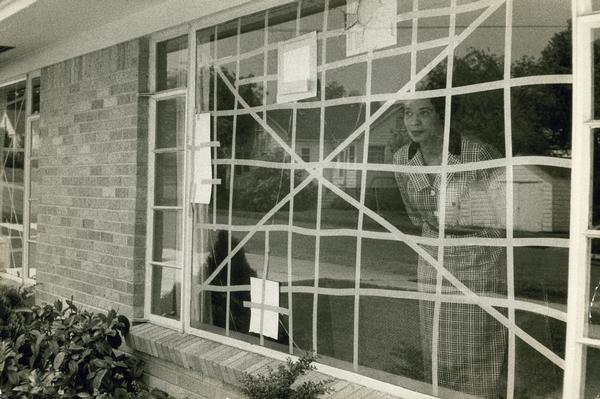 Daisy Bates peering through the broken window repaired with tape.