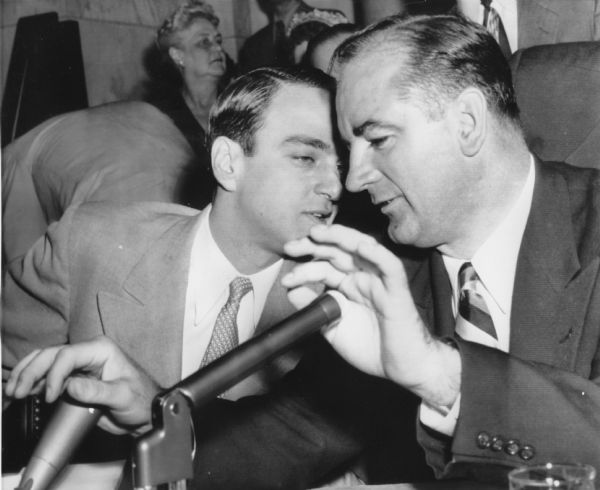 During the first day of the Army-McCarthy Hearings, Senator Joseph R. McCarthy holds both hands over the microphones while speaking with counsel Roy Cohn.