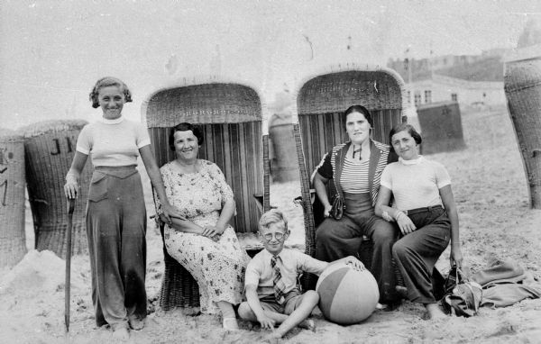A family at the beach in Holland.Two are sitting in beach chairs. There is a child wearing glasses sitting in the sand next to a beachball.