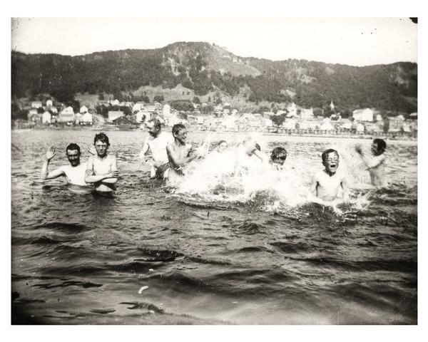 A group of men and boys swimming and splashing in the Mississippi River. Alma can be seen in the background.