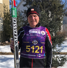Author Jerome Poling standing outdoors in winter holding cross-country skis, wearing a 2021 American Birkebeiner race bib and ski gear.