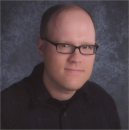 Author James Nelsen wearing black glasses and a black shirt, and pictured in front of a grey background.