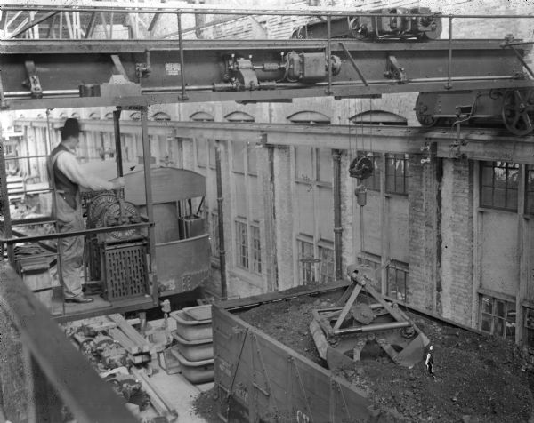 A crane operator looking down on coal car near exterior of building.