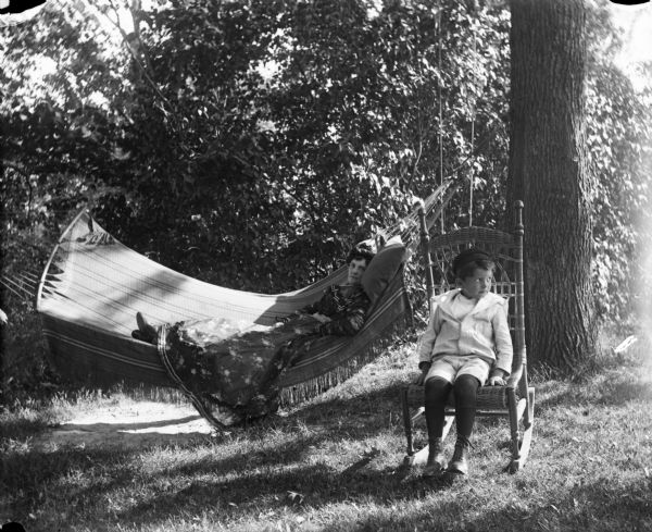 A boy in a cane chair, next a hammock with a woman lounging.