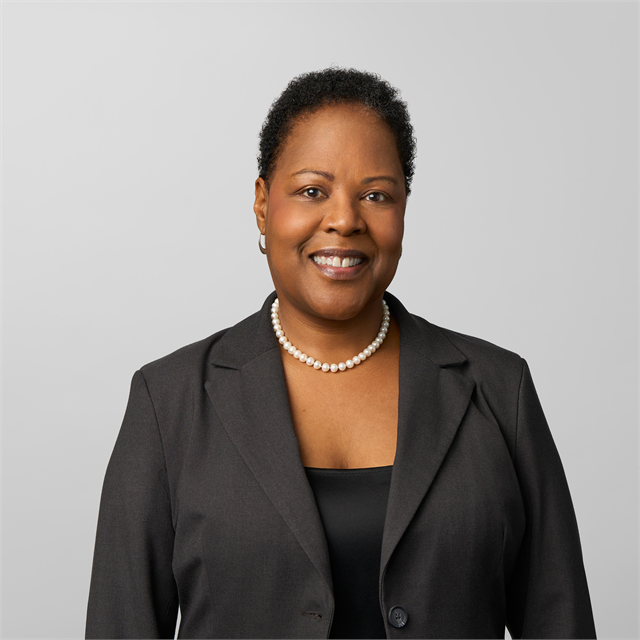 Photograph of Melanie Adams, a smiling African American women with short curly hair wearing a black blazer, black blouse, and pearls