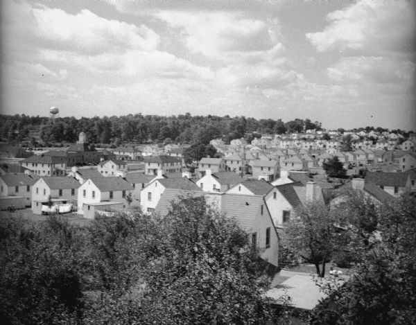 Elevated view over trees of village. A water tower is visible on a hill with trees in the background.