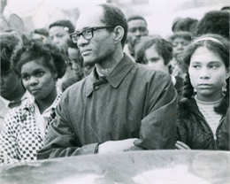 Loyd Barbee stands with his arms crossed with a somber crowd of young African Americans.