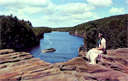 A woman in an Indian dress sits on High Rock overlooking a tour boat on the Wisconsin River.