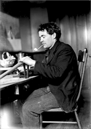 Portrait of the photographer J. Robert Taylor sitting at a table smoking a pipe and possibly woodworking.