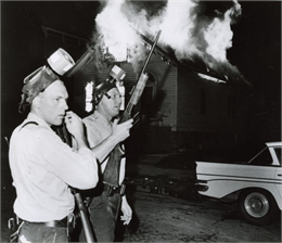 Freedom House in flames after Milwaukee Police fired tear gas into the building. Two armed officers stand in front of the burning building. Both officers have gas masks on their heads. WHI 48147.