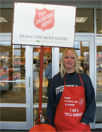 A female Salvation Army bell ringer poses outside Shopko. Apron reads; "need knows no season - I am a bell ringer."