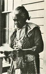 An elderly black woman reading a pamphlet on her porch.