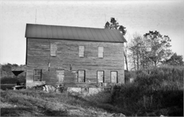 A view of a mill with a stone foundation on an overgrown site.