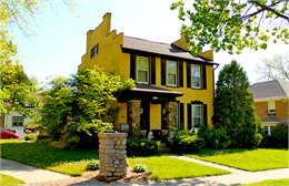 Exterior of yellow brick Federal style colonial house with brick parapets and chimneys rising above the roof line.