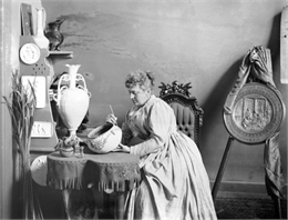 Artist at a table painting a ceramic bowl.