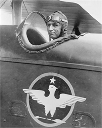 General William Mitchell wearing aviator goggles piloting an early military airplane.