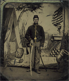 Full-length studio portrait of a civil war soldier with an american flag, cannon and tent in the background.
