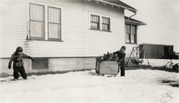 Young Richard and Ralph Quinney hauling firewood on a sled through the snow past the farmhouse.