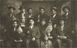 Posed studio group portrait in front of a painted backdrop of Winnebago Indian men and one young woman. Each of the men is holding a mounted bird of some species.