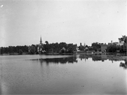 View across Lake La Belle toward lakeside factories, residences, and churches.