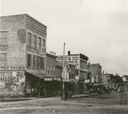 A view of a cluttered Monroe street. The corner building later became Schuetze's Clothing Store.