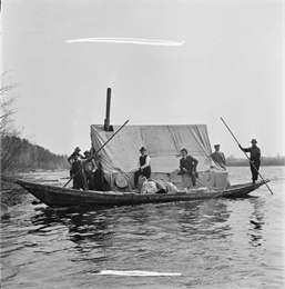 Eight men are in a boat driving logs down the Wisconsin River.