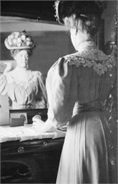 Indoor portrait of Mary E. Smith looking at her reflection in a vanity mirror while opening a jewelry box.