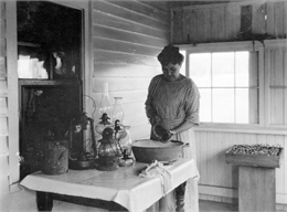 Woman cleaning kerosene lamps on the front porch of her house.
