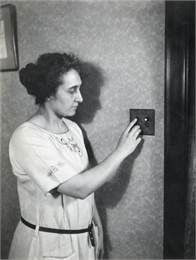 Mrs. Waggoner pushes a button on an electric light switch on the wall in her farmhouse.