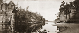 Panoramic view from shoreline of the Wisconsin River in the Wisconsin Dells. A sandy beach area is on the right, and rock formations are on both sides of the river.