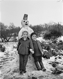 Winter scene with children posing in front of a snowman.