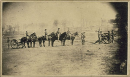 Soldiers of the 3rd Wisconsin Artillery at Camp Randall man a cannon on wheels while other men on foot and on horseback follow.