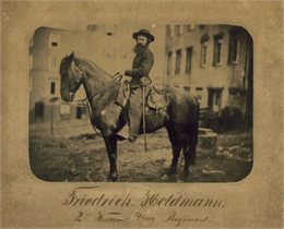 Friedrich Holdmann of the Second Wisconsin Cavalry Regiment during the Civil War, astride his horse. Buildings are in the background.