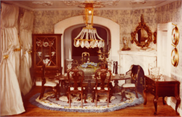 Doll house dining room with miniature dining table, Queen Ann chairs, chandelier, curtains, fire place, mirror and china hutch.