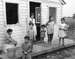 A Mexican woman and her six children stand on the porch of the multiple-family housing provided to them by the pea cannery for which their husband and father works.