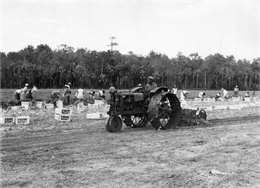 African American field worker levels the ground with a McCormick-Deering F-12 tractor and a rotary scraper.