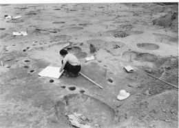 A historic black and whtie photo of a woman mapping features at an archaeological site.