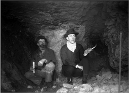 Interior of a lead mine showing two miners kneeling with candles in their hands.
